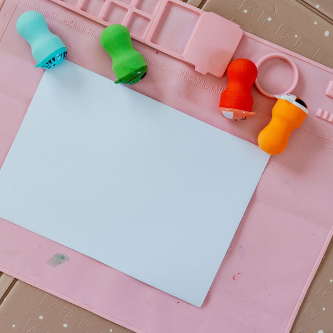 Colorful paper clips on a pink cutting mat with a white sheet of paper.