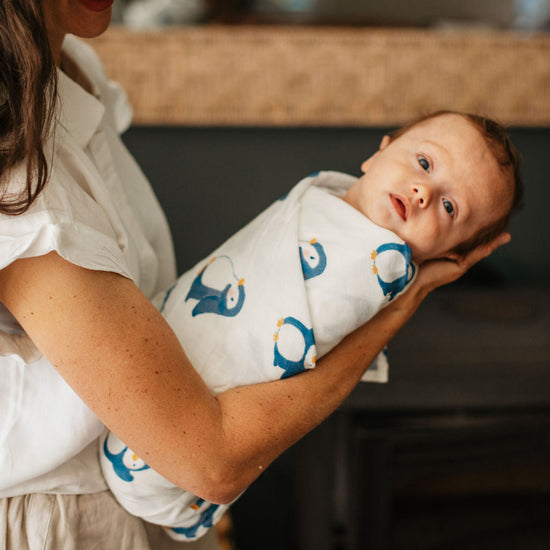 Woman holding a baby wrapped in a blanket with penguin design in a kitchen setting