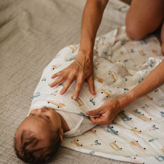 Person adjusting a baby wrapped in a blanket with animal prints on a wooden floor.