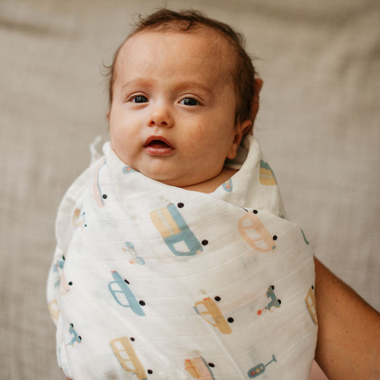 Baby wrapped in a patterned blanket with a neutral background