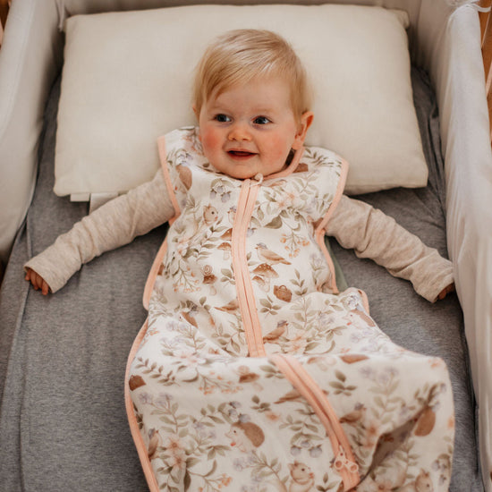 Baby lying in a crib wearing a floral sleep bag with a neutral color scheme.