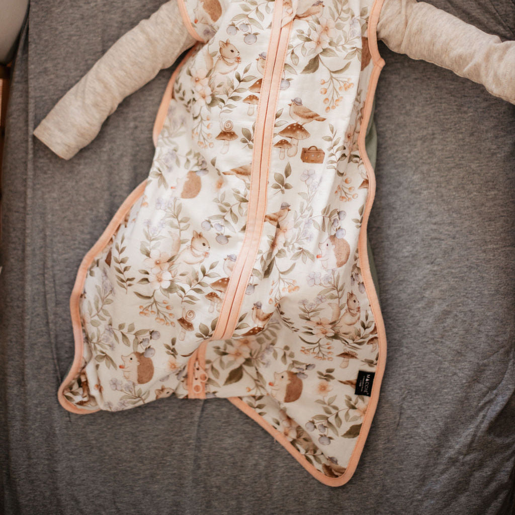 Baby lying on a gray surface wearing a patterned onesie with a zipper.