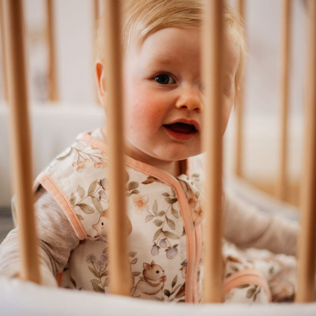 Baby peeking through wooden crib bars with a floral outfit