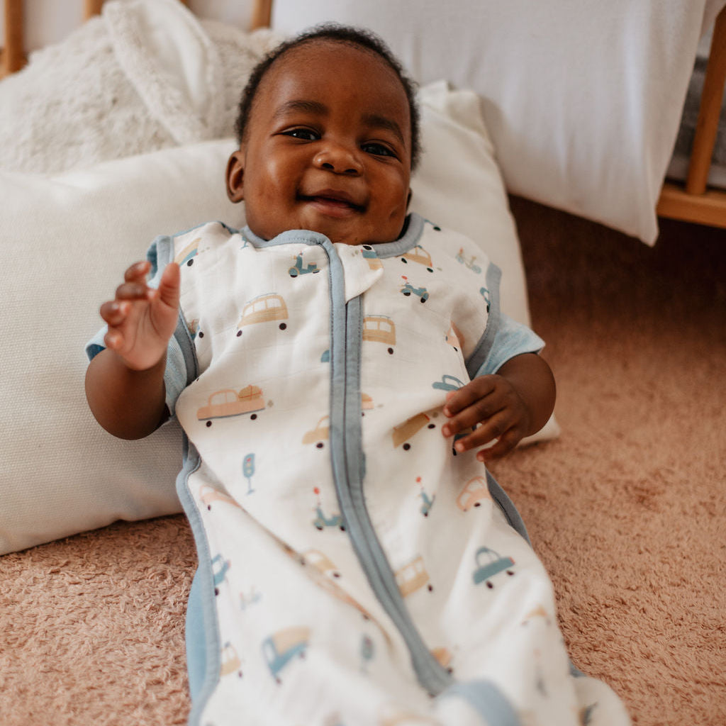 Baby in a patterned onesie sitting on a carpeted floor.