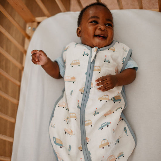 Baby in a patterned onesie lying on a white blanket in a crib.