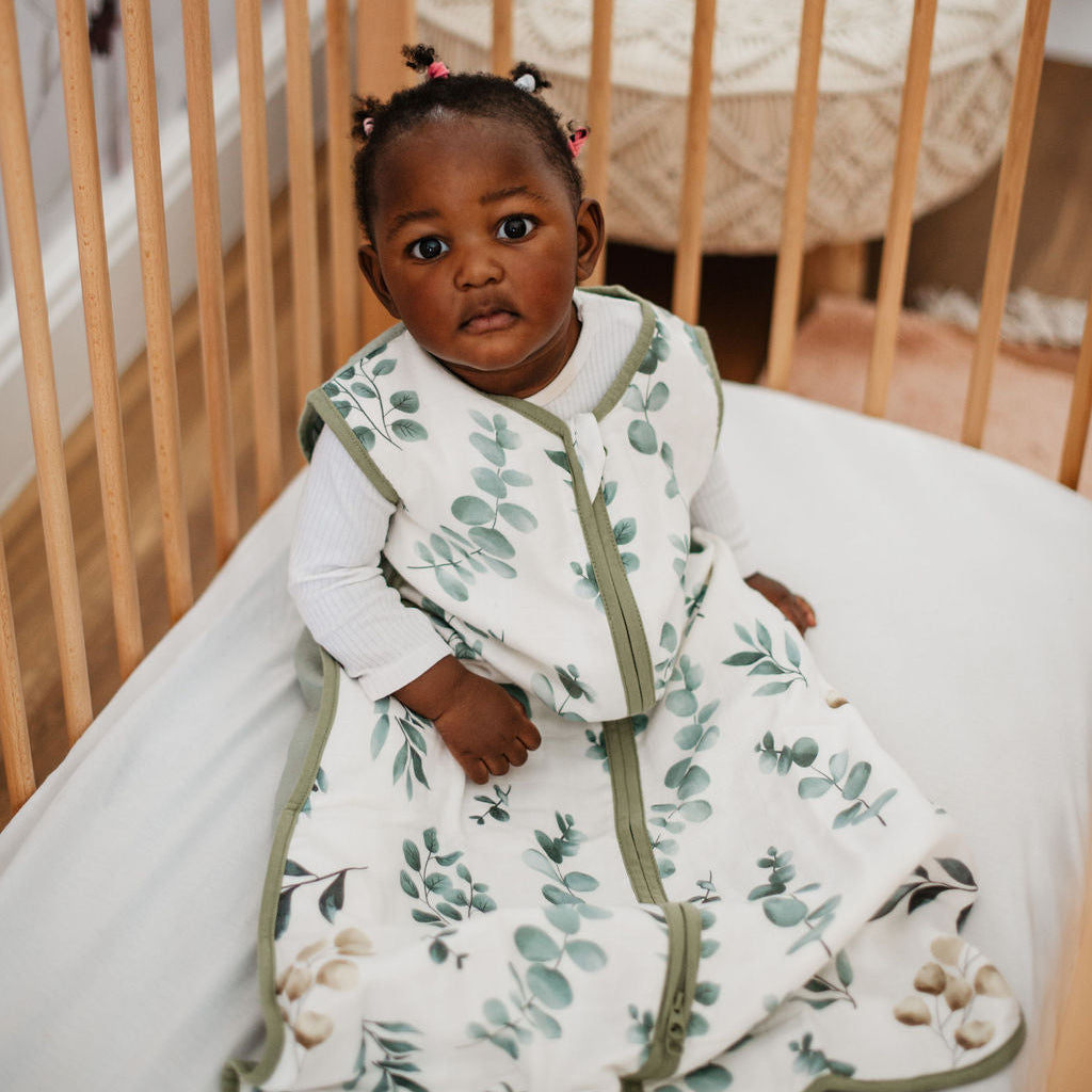 Baby in a crib wearing a white and green patterned outfit.