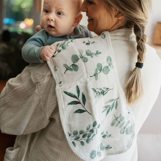 Woman holding a baby in a sling with a green leaf pattern