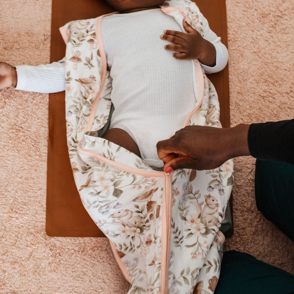 Baby lying on a mat with a floral blanket, being measured by an adult.