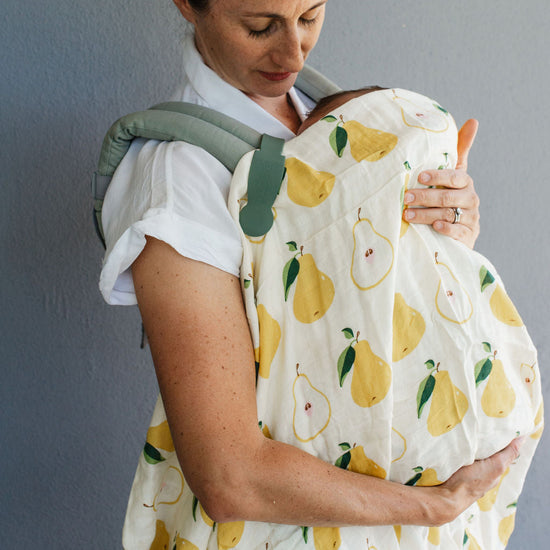 Woman holding a baby in a carrier with a white and yellow pattern against a gray background