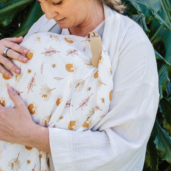 Woman holding a baby wrapped in a floral wrap against a green leafy background