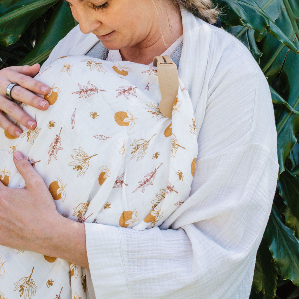 Woman holding a baby wrapped in a floral wrap against a green leafy background