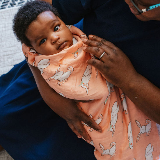 Person holding a baby wrapped in a peach-colored blanket with dog patterns on a textured surface.