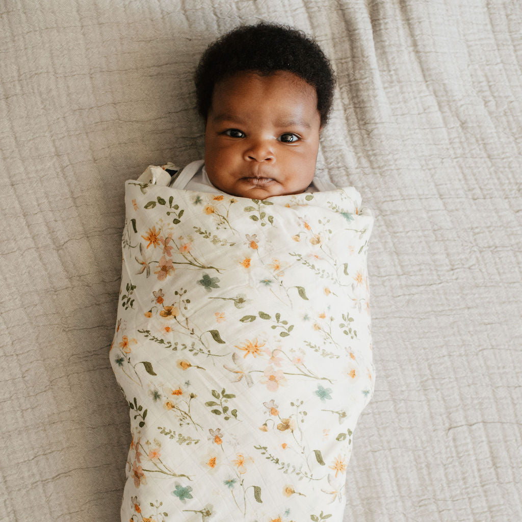 Newborn baby swaddled in a floral blanket on a textured surface