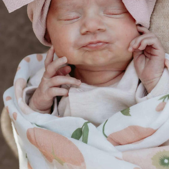 Newborn baby wrapped in a floral blanket with a large pink bow on its head.