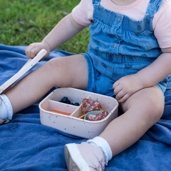 Child sitting on a blue blanket outdoors with a bento box