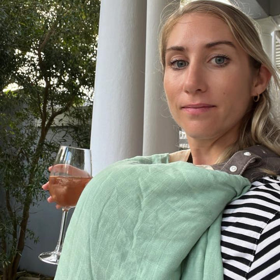 Woman holding a glass of wine and wrapped in a green blanket on a porch.