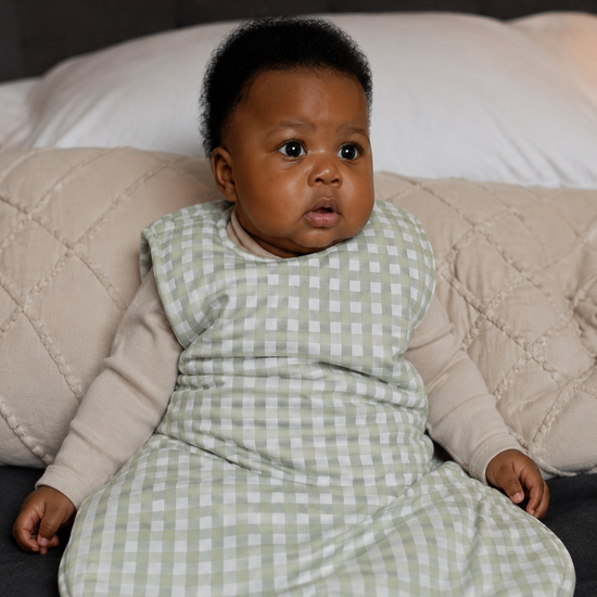 Baby in a green checkered outfit sitting on a couch