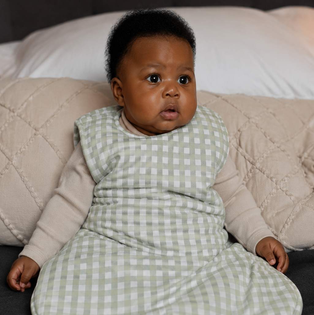 Baby in a green checkered outfit sitting on a couch