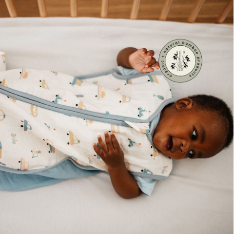 Baby in a patterned swaddle lying on a bed with a visible brand logo.