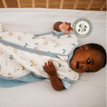 Baby in a patterned swaddle lying on a bed with a visible brand logo.