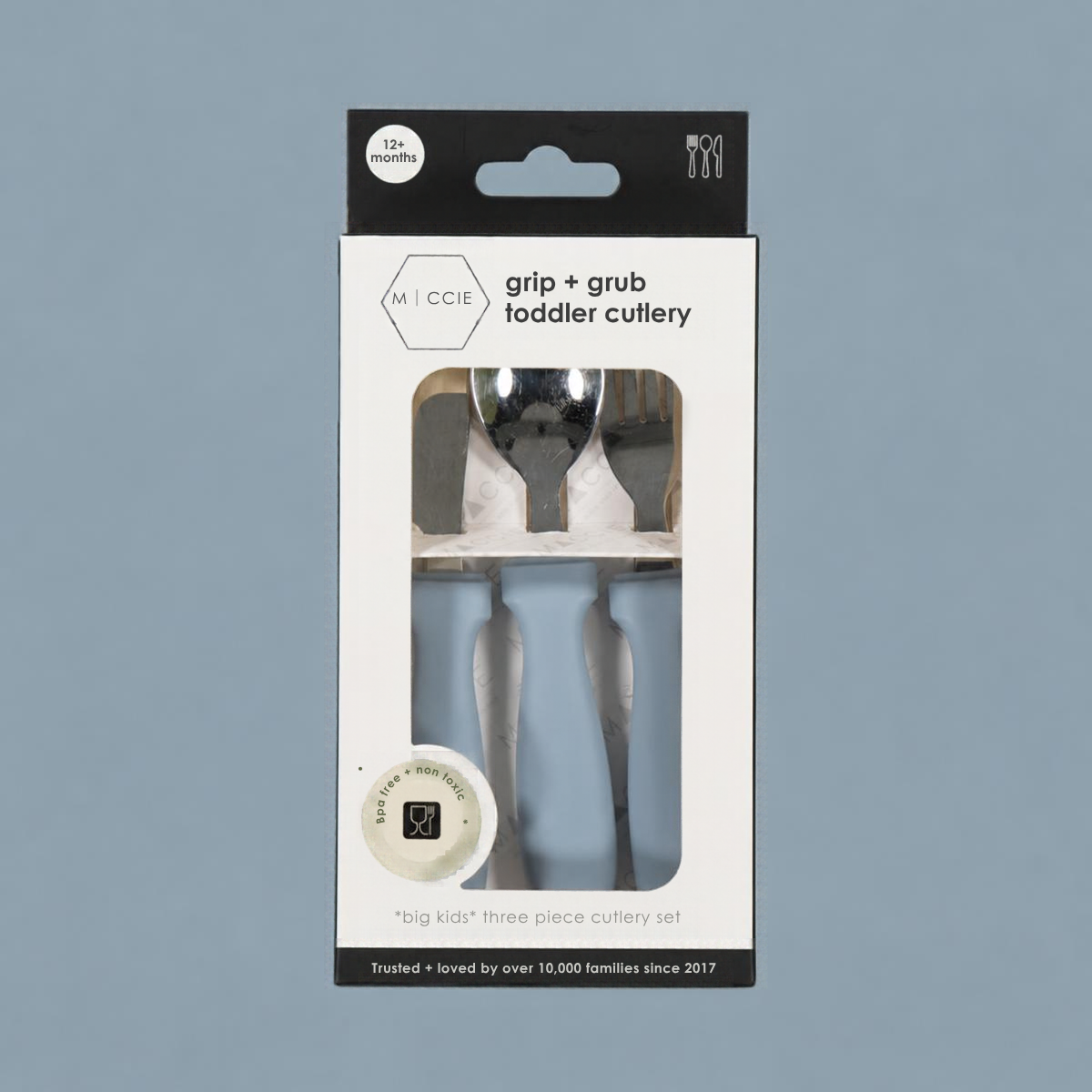 Miccie grip + grub toddler cutlery in its original retail packaging, featuring a three-piece stainless steel spoon and fork set with light blue silicone grips, shown against a solid slate blue background.