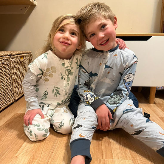 Two children in pajamas sitting on a wooden floor.