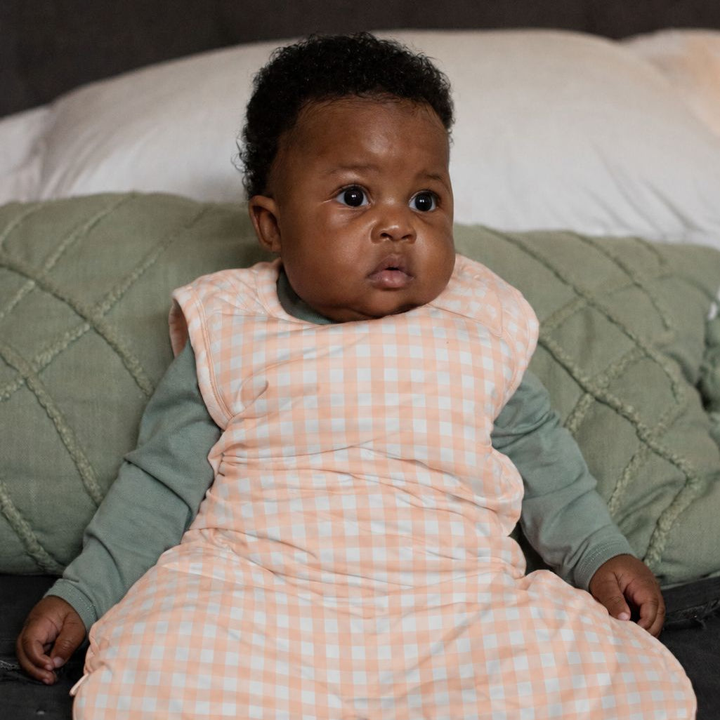 Baby in a pink checkered outfit lying on a bed with green blanket