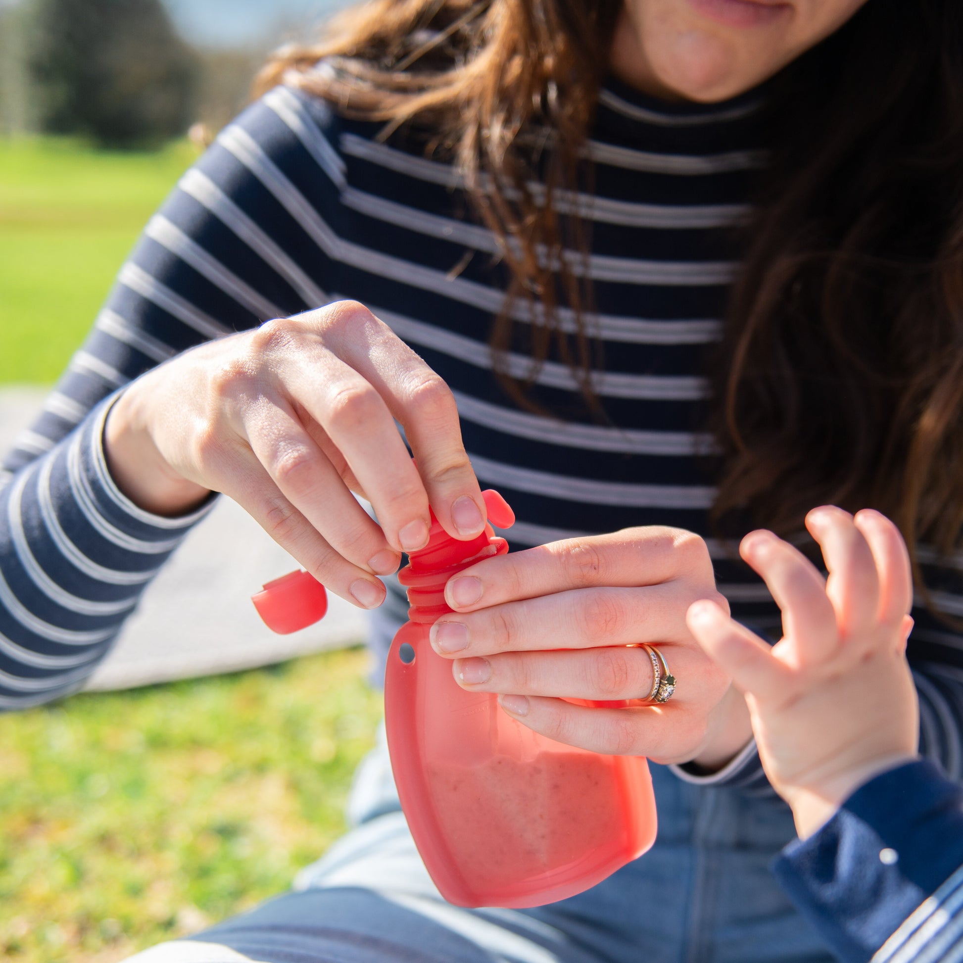 Woman and child outdoors with a red object, possibly a toy or bottle.