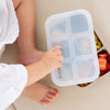 Person holding a white compartmentalized container with colorful snacks on a beige surface
