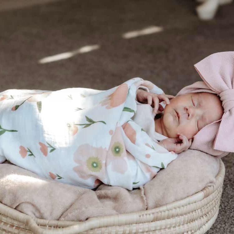 Newborn baby swaddled in a floral blanket with a large pink bow on a textured surface
